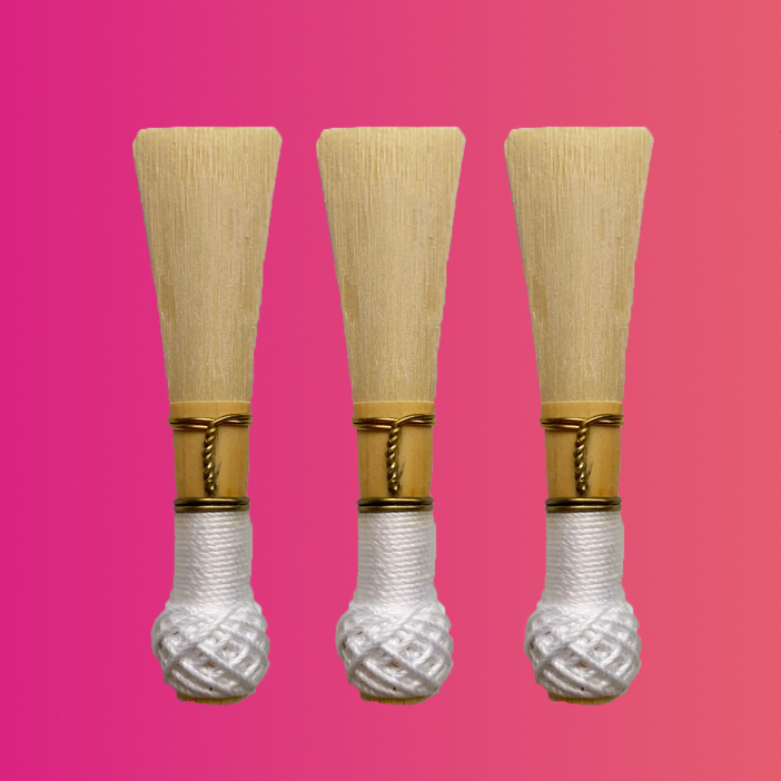 three bassoon reeds with white binding on pink background